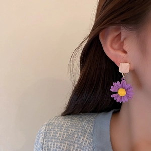 Detailed view of pink square stud and purple daisy flower earrings on a model