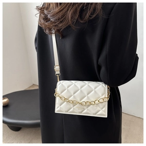 Detail of white quilted crossbody bag with golden chain strap on model's shoulder