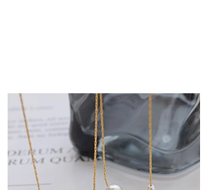 Close-up of a gold thin chain necklace with two elegant white pearl pendants on textured paper