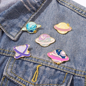 Set of five colorful planet enamel pins pinned on a blue denim jacket pocket