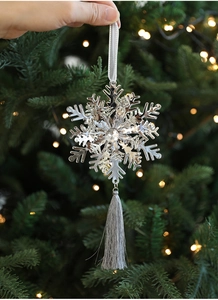 Close-up of silver metal snowflake ornament with tassel on a Christmas tree background