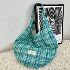 Détail d'un sac à bandoulière en toile à carreaux bleu et vert avec étiquette blanche