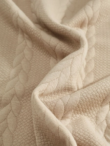 Close-up of beige knit fabric with detailed leaf-shaped jacquard quilting patterns