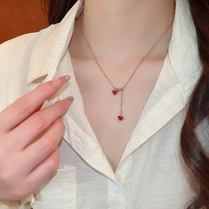 Close-up of a gold necklace with two red heart pendants worn by a model in soft light