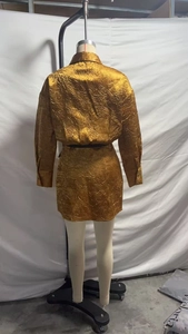 Detail van een gouden satijnen jurk met geplooide textuur en glanzende metallic stof