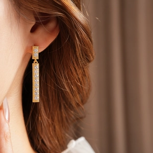 Gros plan de boucles d'oreilles pendantes dorées avec zircons carrés portées par un mannequin