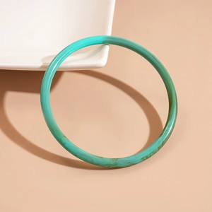 Macro shot of turquoise marble acrylic bangle resting on white ceramic plate edges