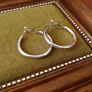 Macro shot of silver hoop earrings on green velvet cushion with vintage gold frame