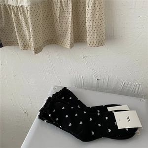 Detail of black crew socks with white heart patterns and elegant ruffled edges on white surface