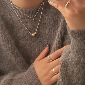 Minimalist double gold ball necklaces layered on grey knitwear with sleek rings