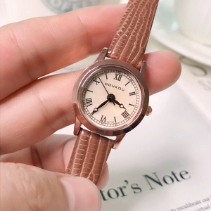 DOUKOU women's brown leather watch with rose gold case on a vintage book background