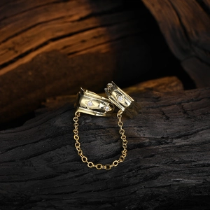 Elegant gold chain earrings with star engravings and zircon stones on charred wood background