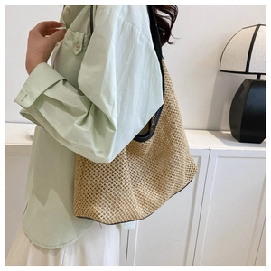 Detail of woven straw tote bag featuring mesh knit design and black leather shoulder strap