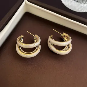 Elegant gold and white C-shaped hoop earrings with marble enamel finish on a display box