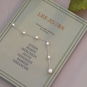Artistic detail of Y-shaped freshwater pearl necklace on a French book cover with green leaf
