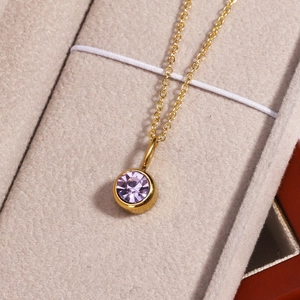 Detailed close-up of a golden necklace featuring a round purple gemstone pendant in a jewelry box