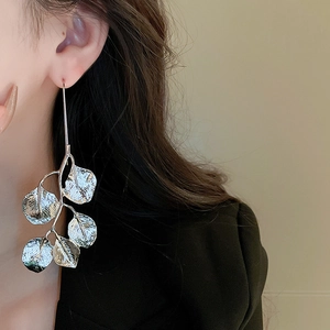 Detailed view of silver leaf-shaped metal earrings worn by a model in a natural setting