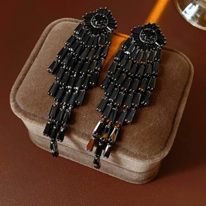 Detail view of black tassel earrings with geometric beads on brown velvet jewelry box