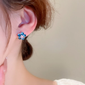 Macro shot of a tiny blue crystal flower earring with a small center diamond on ear