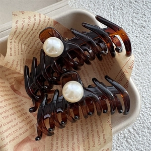 Detail of two tortoiseshell hair claws with pearl accents on a vintage paper background