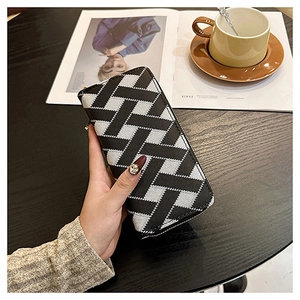 Close-up of hand holding black and white woven pattern wallet on a cafe table