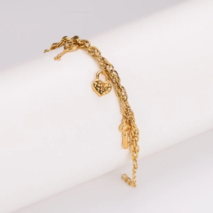 Bracelet doré en acier inoxydable avec breloques cadenas cœur et clé sur support blanc
