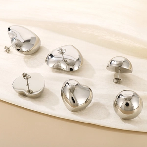 Poliertes Edelstahl Herz und Kugel Ohrstecker Set auf beigefarbenem Satin Hintergrund