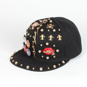 Detailed close-up of a black snapback cap featuring gold rivets, gems and a red kiss logo