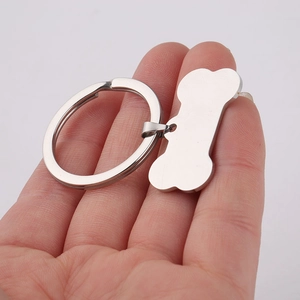 Polished bone-shaped stainless steel pet ID tag and keychain held in hand for size comparison