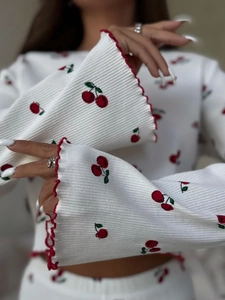 Detail of white ribbed knit pajamas with cherry print and red wavy lettuce edge trim