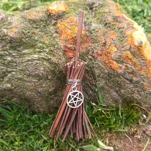 Close-up of decorative mini witch broom with natural twig handle and silver star pendant