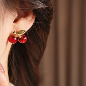 Elegant dark red resin cherry earrings with gold leaf and green zircon worn by a model