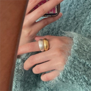 Detail of chunky brushed silver and gold rings worn on a hand with a blue sweater
