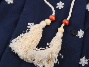 Detail eines blauen Stickkleides mit beigen Baumwollquasten und roten Holzperlen
