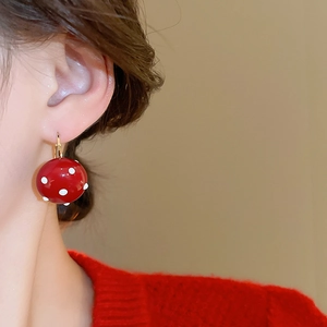 Close-up of a red polka dot spherical earring with gold plated hoop worn by a model