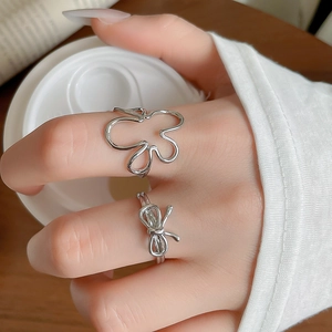 Gros plan d'une bague fleur en argent et bague nœud portées à la main près d'un café