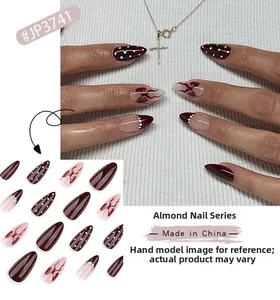 Detail of short almond press-on nails with burgundy bow designs and polka dot accents
