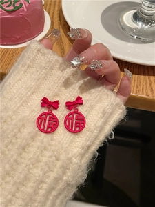 Detail of red bow stud earrings with Fu character pendant on soft knit background