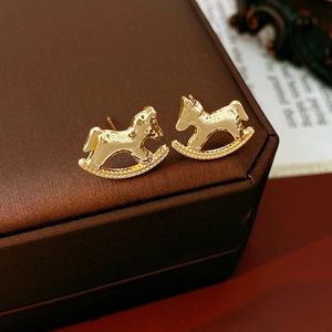Detail shot of gold rocking horse earrings with zircon and pearls on a jewelry box