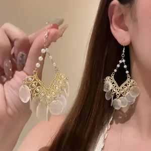 Detail of bohemian gold hollow butterfly earrings with white pearls and shell pendants