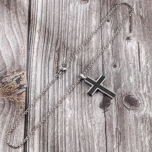 Macro detail of silver and black cross pendant on textured dark wooden surface