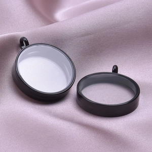 Macro shot of two black stainless steel round bezel pendants on pink silk fabric background