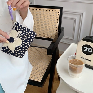 Close-up of small blue polka dot pouch with white flower and purple wrist strap