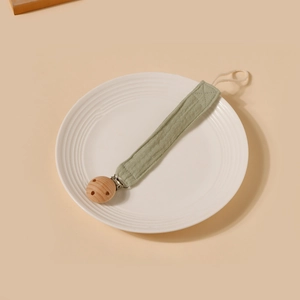Détail de l'attache-tétine en gaze de coton vert clair sur une assiette en céramique