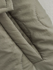 Macro shot of olive green quilted nylon fabric with wavy stitching detail on the jacket