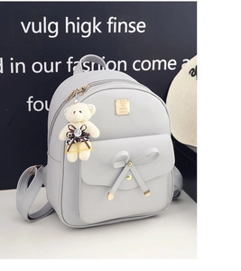 Close-up of light gray PU leather backpack with bow decor and cute bear pendant