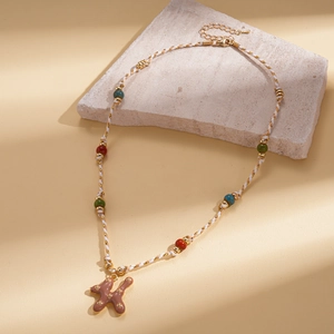 Détail du collier de perles avec pendentif lettre K et accents colorés sur pierre