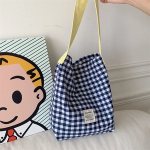 Gros plan du sac cabas en toile à carreaux bleu et blanc avec anses jaunes et étiquette