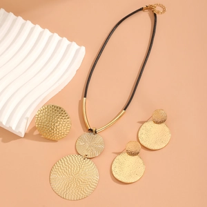 Hammered gold round pendant necklace and matching disk earrings jewelry set on peach background