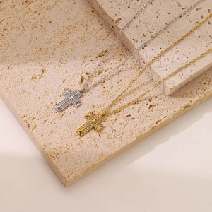 Gold and silver cross necklaces with inlaid zircon on a beige stone surface